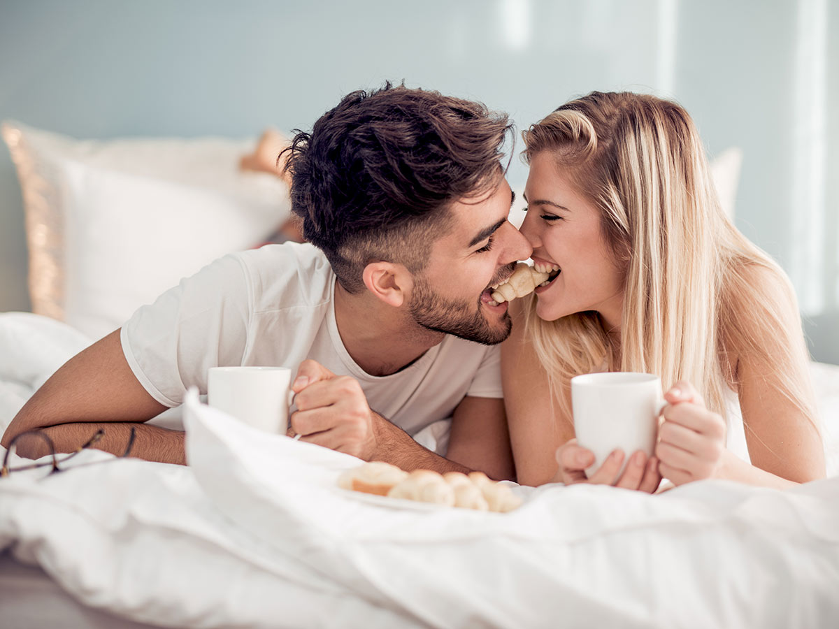 Dating couple enjoying breakfast on the bed as quality time together